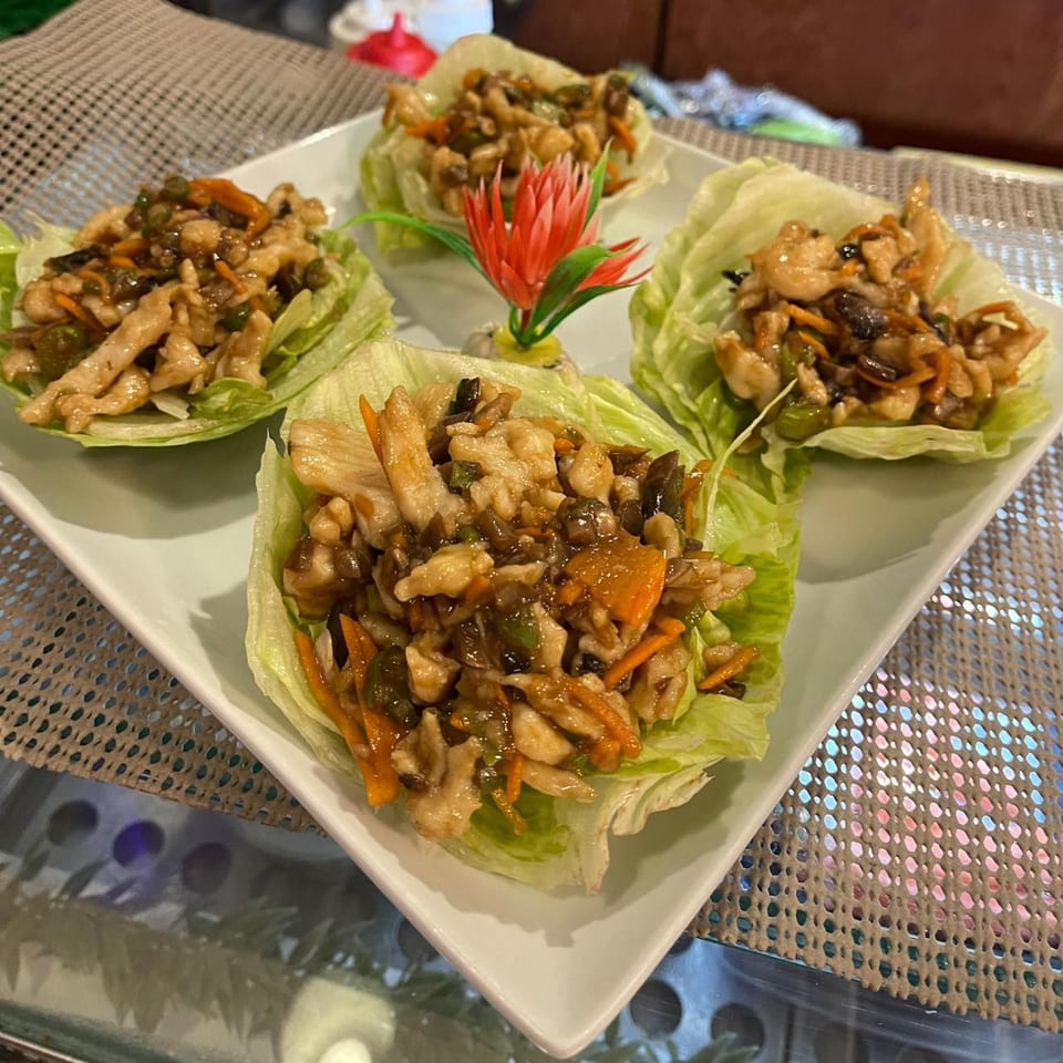Four lettuce wraps filled with chicken, carrots, and mushrooms, garnished with a red flower.