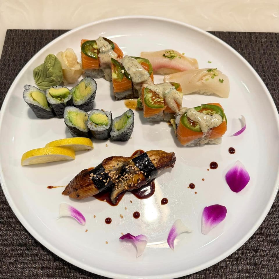 A white plate with various sushi rolls, nigiri, eel, wasabi, ginger, and lemon slices.